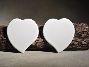 Zwei Prozellanherzen mit Spitze nach links und rechts vor einem Astabschnitt